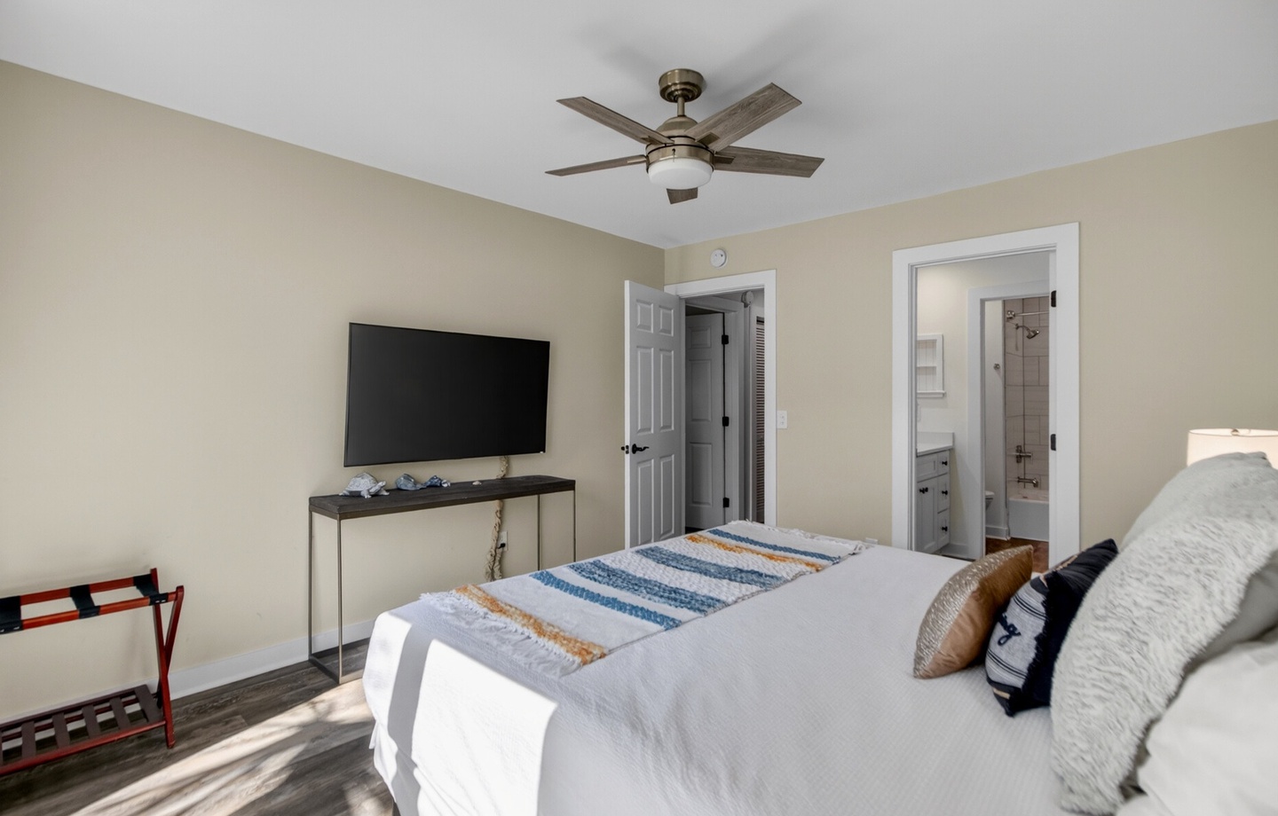 Relax in your bright, airy bedroom featuring a ceiling fan and flat-screen TV. The ensuite bathroom is just steps away for your convenience.