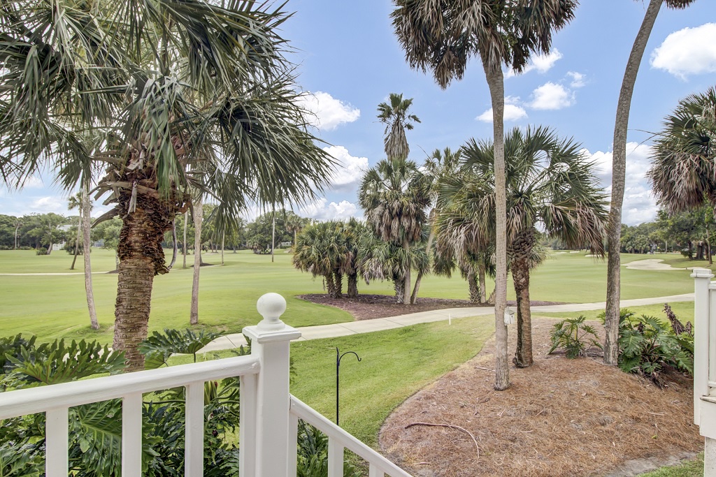 Peaceful view of a golf course framed by palm trees, seen from a charming white railed porch.