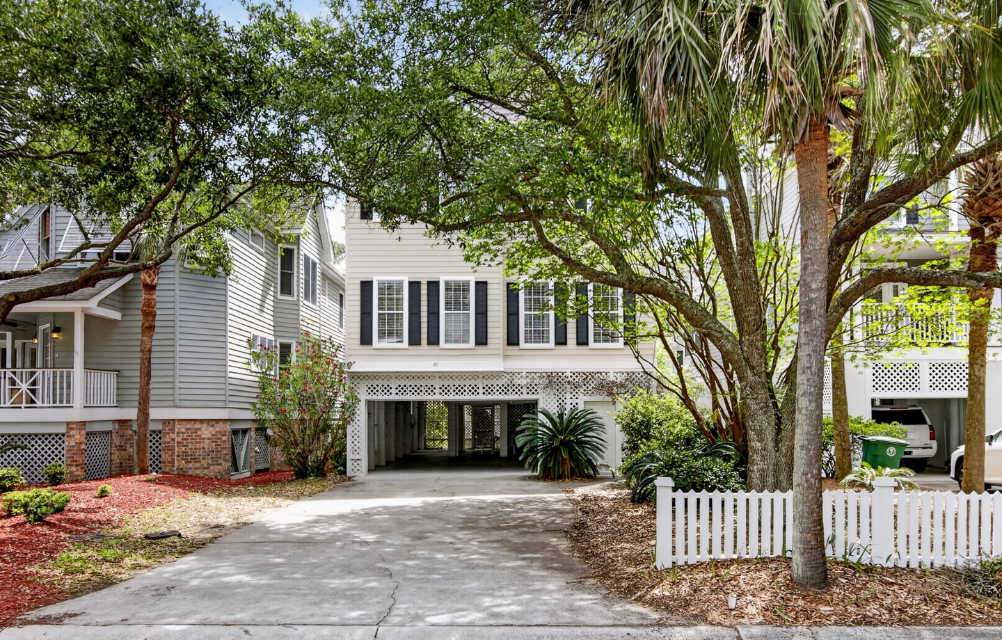 Classic coastal home framed by lush oak trees and palms, offering covered parking and a peaceful neighborhood setting for your beach getaway.
