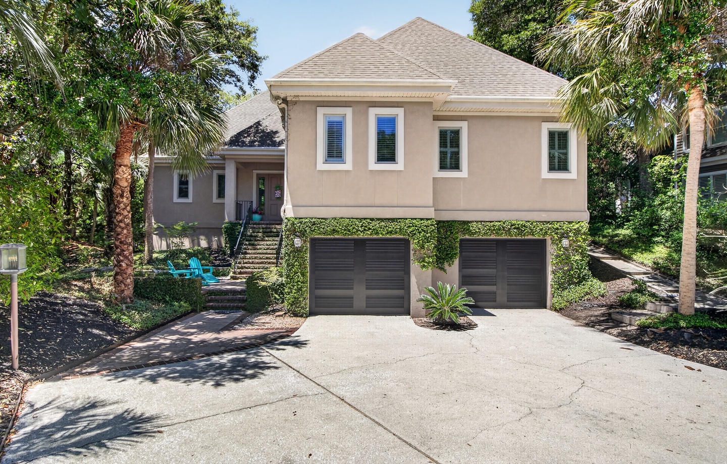 A coastal-style home with two-car garage, nestled among palm trees and lush tropical landscaping in a quiet neighborhood setting.