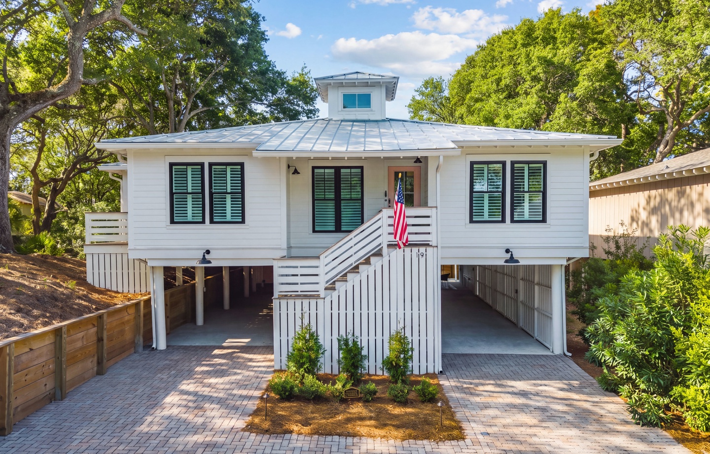 Charming coastal cottage with elevated design, nestled among mature oak trees with convenient covered parking and welcoming front porch entrance.