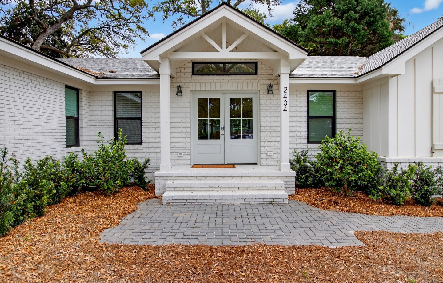Charming white brick home features a welcoming entrance with modern farmhouse details and mature landscaping in a peaceful neighborhood setting.