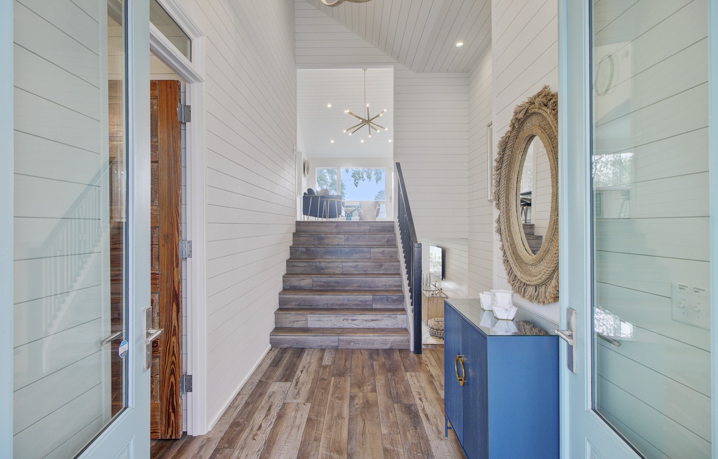 Welcoming entrance hallway with rustic wood stairs leading to your upstairs retreat, featuring coastal-inspired design and natural light.
