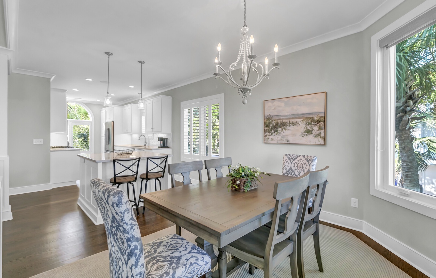 Picture yourself sharing meals at this elegant dining table, bathed in natural light from large windows, while an open kitchen invites easy conversation. The chandelier adds a touch of charm, making every gathering feel special.
