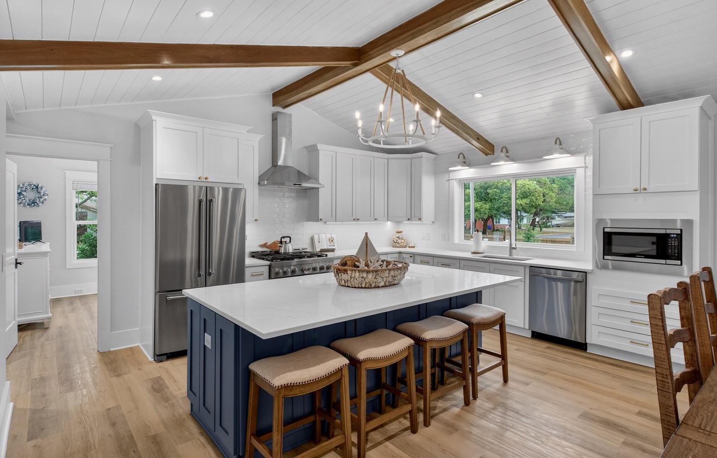 Your spacious chef's kitchen features white cabinetry, navy island with seating, stainless appliances, and beautiful exposed beam ceiling.