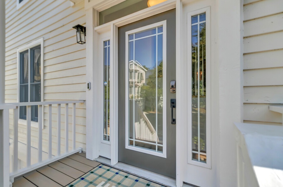 The main entrance features a gray door with decorative glass panels and white trim, flanked by sidelights, leading to a welcoming covered porch with light beige siding.