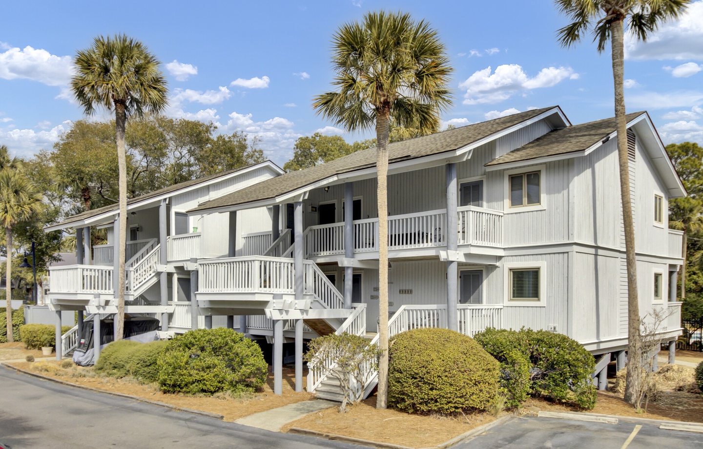 This coastal property features classic gray siding and multiple balconies surrounded by iconic palm trees in a peaceful residential setting.