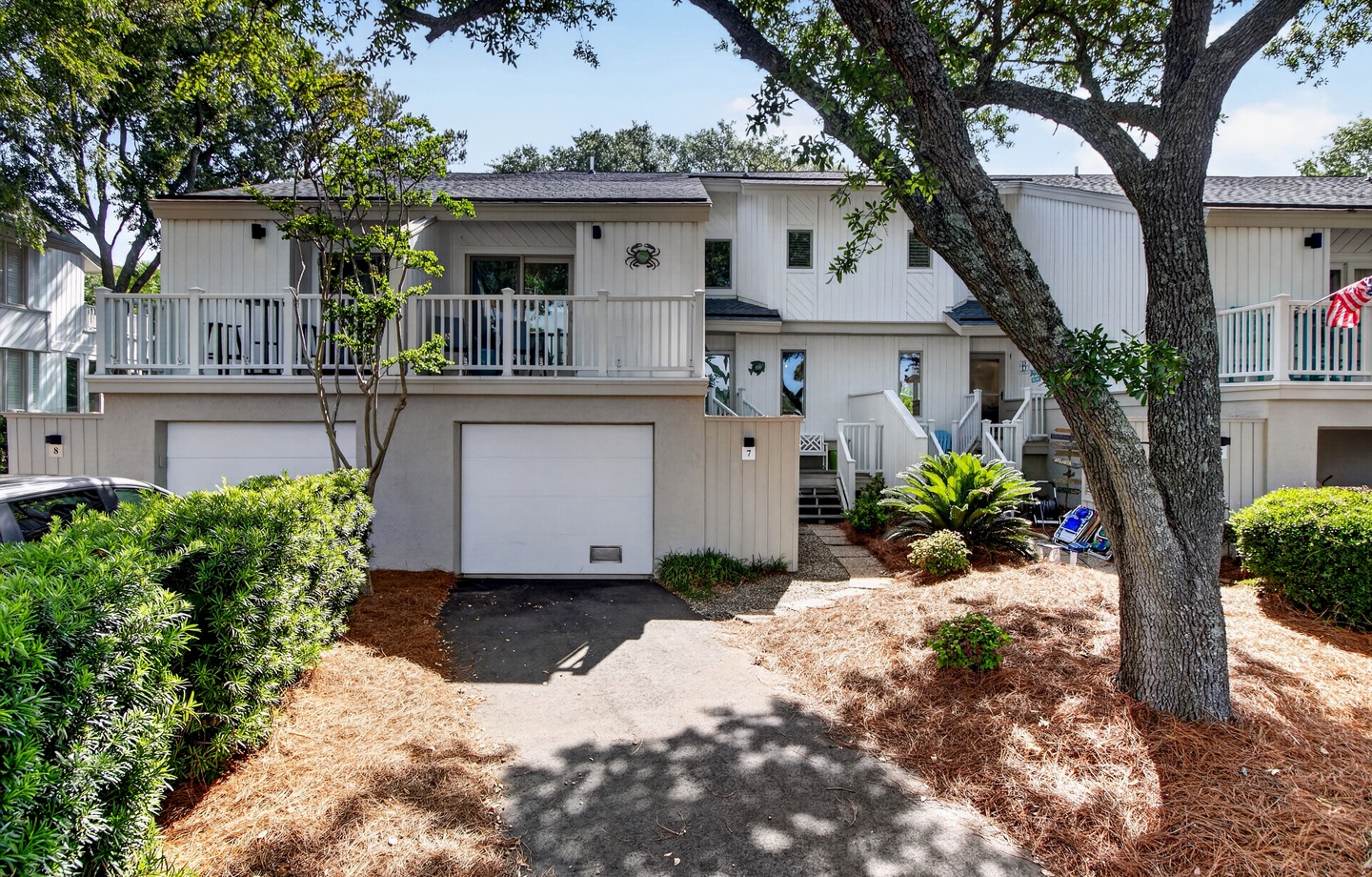 This two-story vacation rental features a private garage and inviting balcony, nestled beneath towering oak trees in a peaceful, landscaped setting.