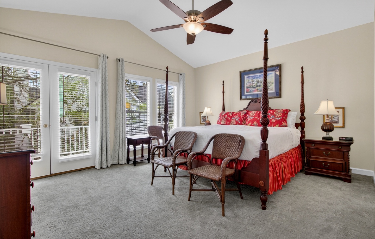 Your spacious bedroom retreat features a stunning four-poster bed with elegant red accents, vaulted ceilings with a ceiling fan, and French doors opening to your private balcony with peaceful views.