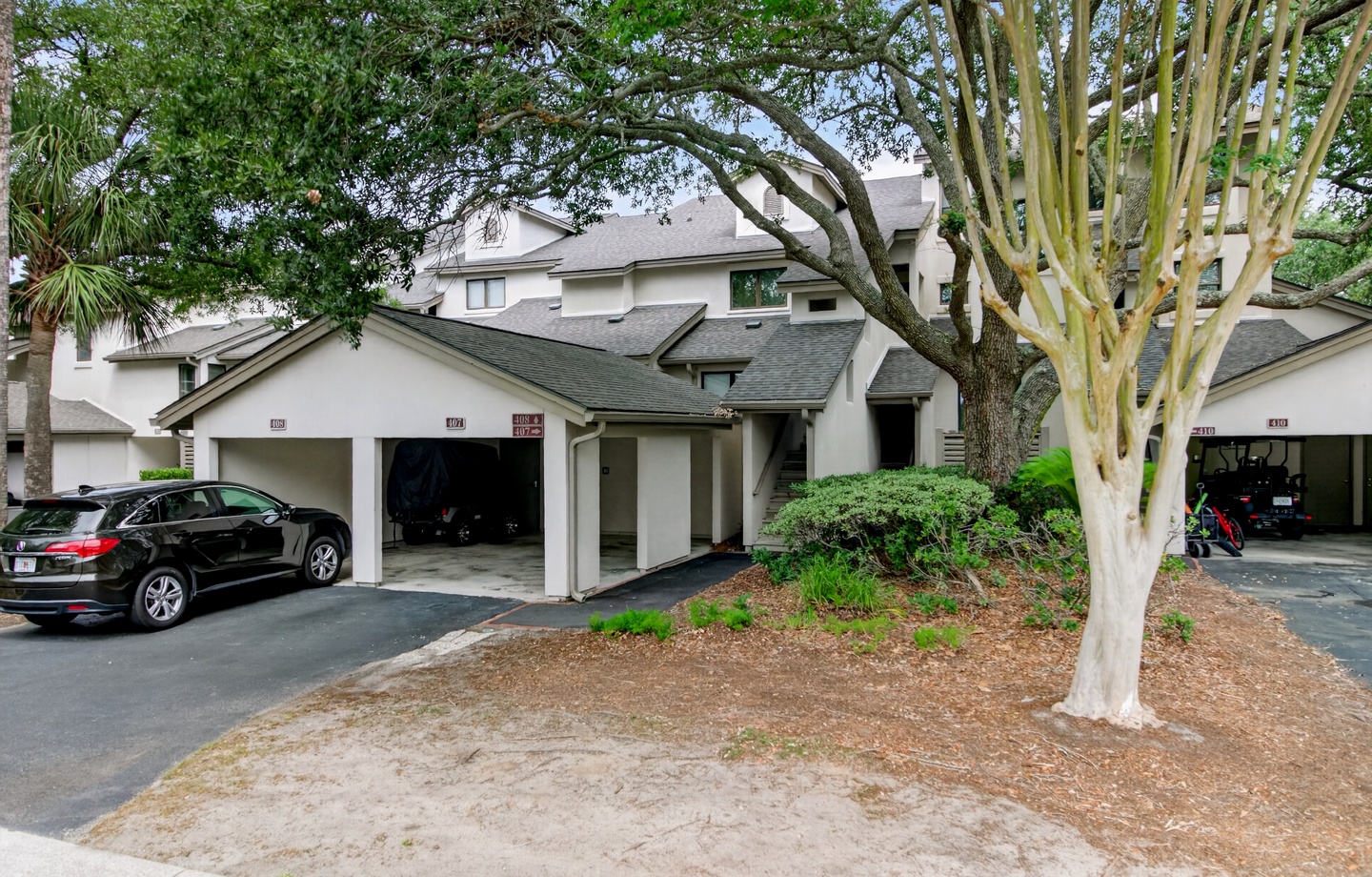 Multi-unit residential property with attached garages, landscaped with mature trees and tropical plantings, providing convenient covered parking for guests.