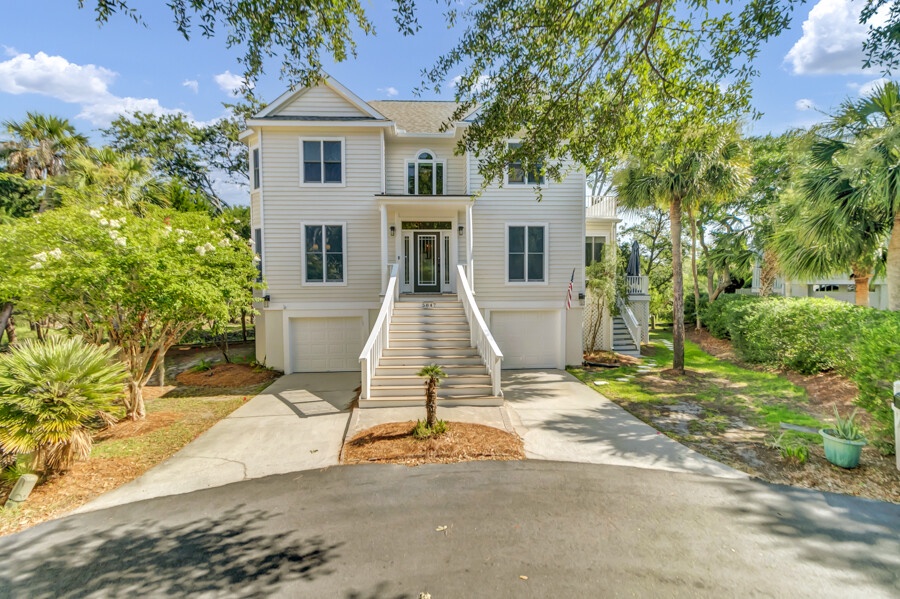 This elegant two-story coastal home features classic architecture with pristine white siding, surrounded by mature landscaping, palms, and lush greenery in a quiet residential setting.