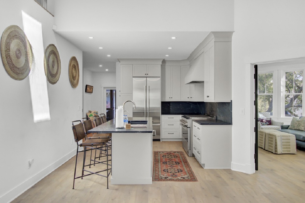 - Chef’s kitchen features stainless steel appliances, gas range, and a deep farmhouse sink - Sleek white cabinetry and dark countertops pair with artistic wall decor - Grab a seat at the island with industrial barstools and cozy rug accents