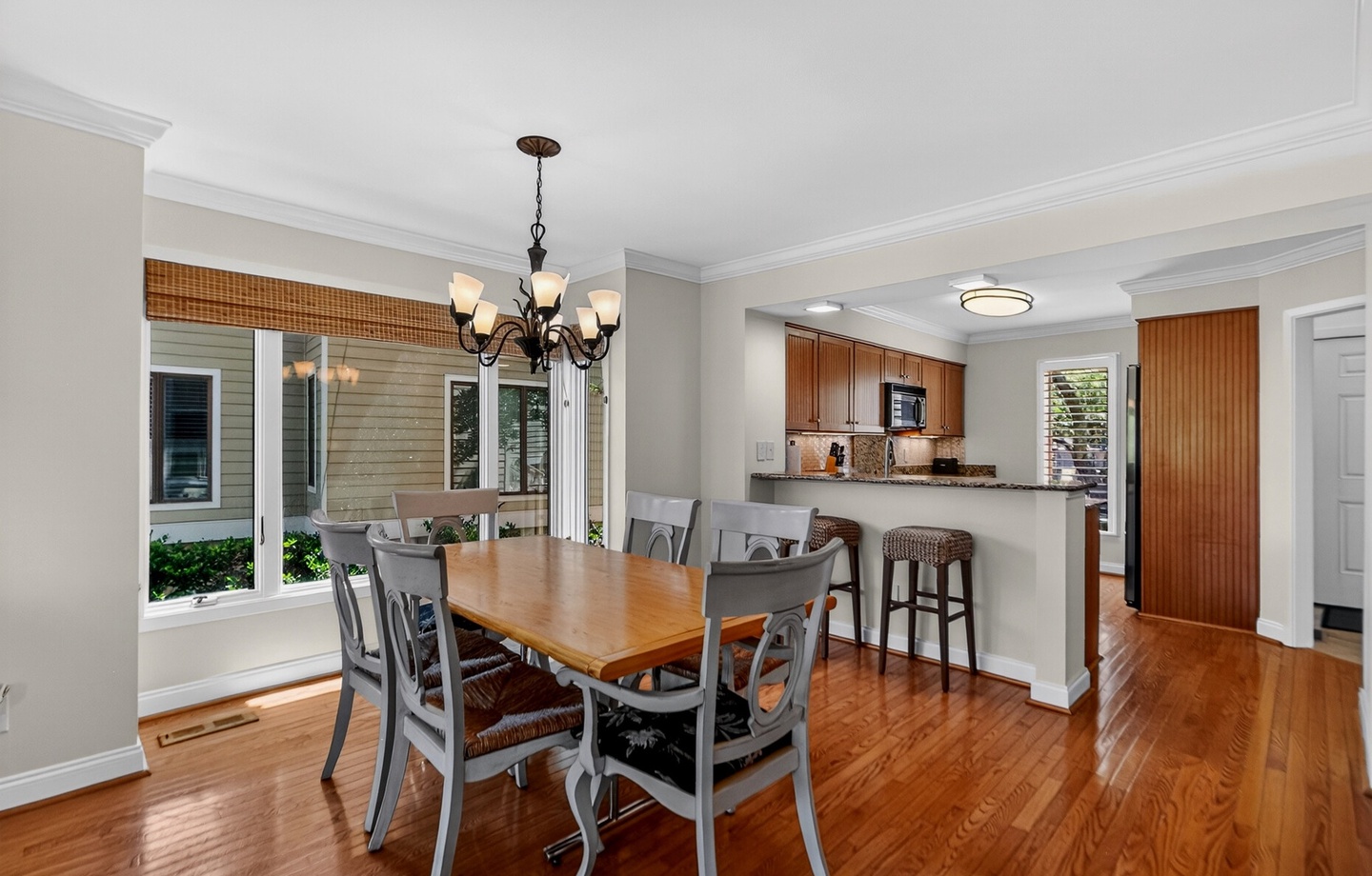 Your open-concept dining and kitchen space features gleaming hardwood floors, a breakfast bar for casual meals, and abundant natural light streaming through floor-to-ceiling windows overlooking the lush greenery outside.