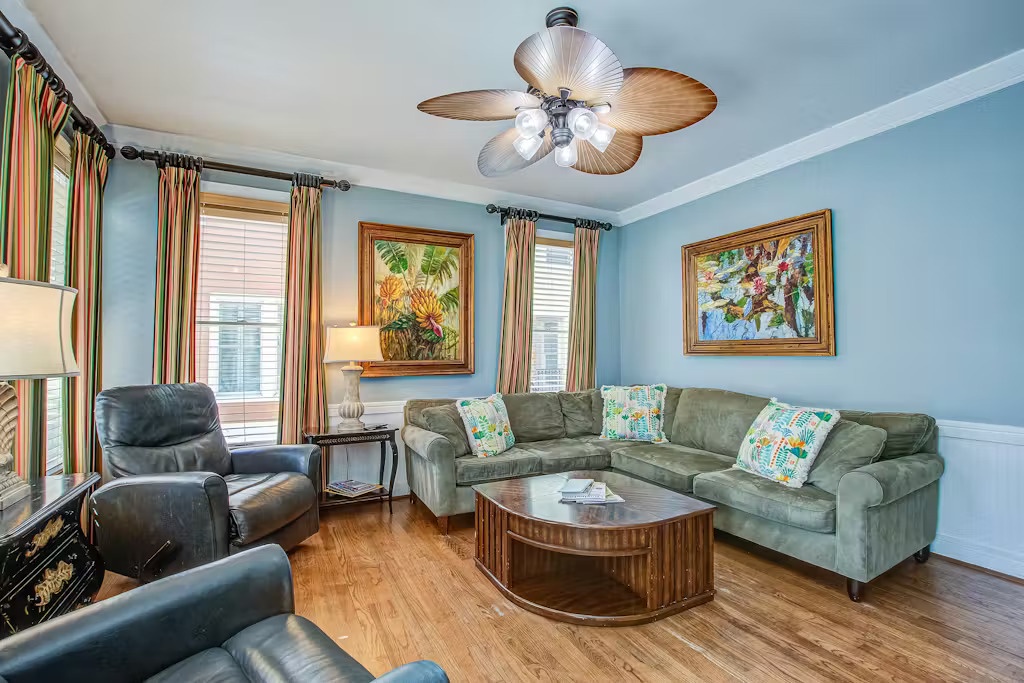 Relax in your bright living room with plush sectional seating, tropical artwork, and a refreshing ceiling fan overhead.