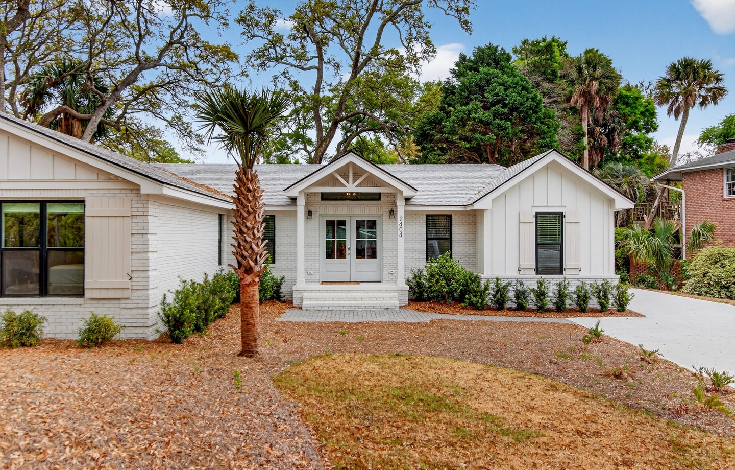 Modern coastal cottage nestled among mature palms and lush landscaping in a peaceful residential setting.