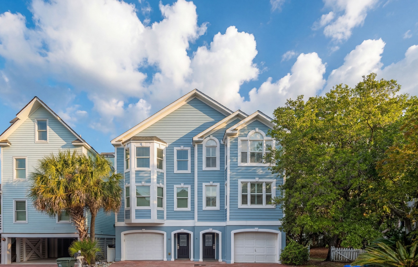 Coastal-style architecture welcomes guests with charming blue siding and white trim, set against swaying palms and a bright Carolina sky.