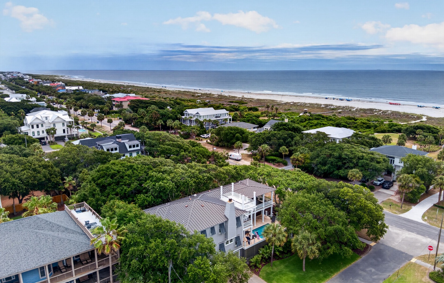 Aerial view of coastal vacation properties nestled among lush greenery with pristine beach and ocean stretching beyond, showcasing the peaceful seaside neighborhood setting.
