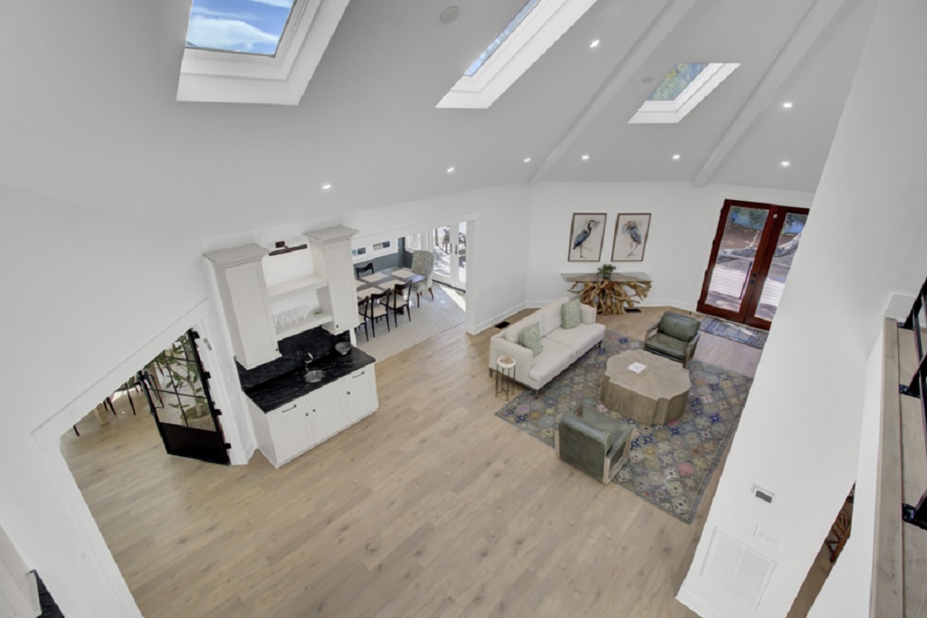 Bright vaulted living space with skylights, white walls, and wood floors for a breezy vibe - Lounge on comfy sofas beneath dramatic ceilings and modern lighting - Seamless open layout flows from sitting area to dining and kitchen zones