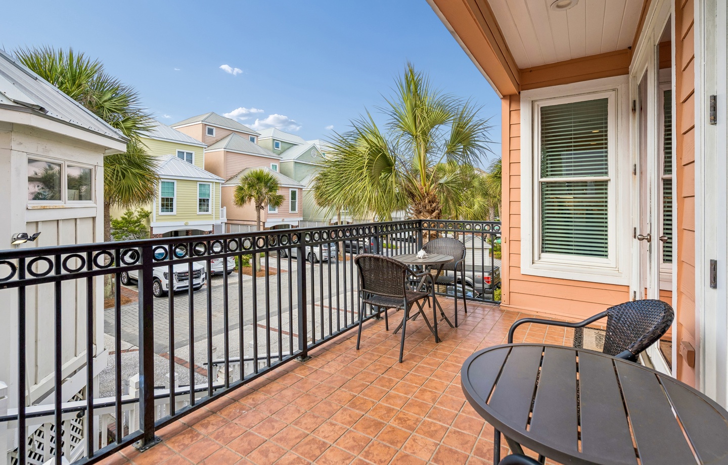 Step onto your private balcony with charming bistro seating, where tropical palms frame colorful neighborhood views under endless blue skies.