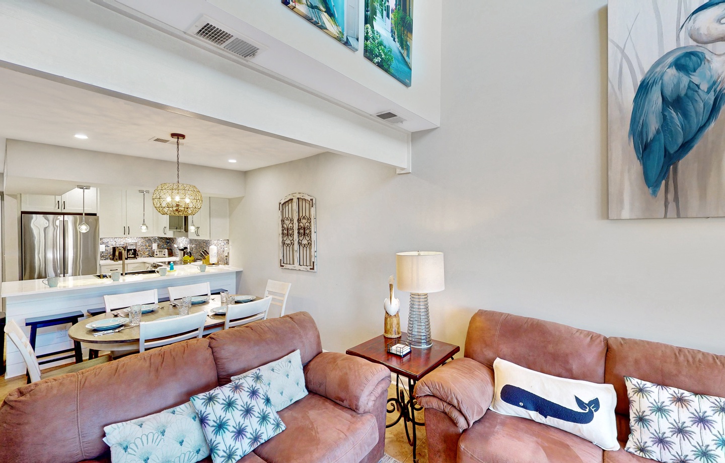 An open living space flows into a bright dining area and modern kitchen, creating a welcoming home-away-from-home. Soaring ceilings and coastal artwork add a sense of calm and space.