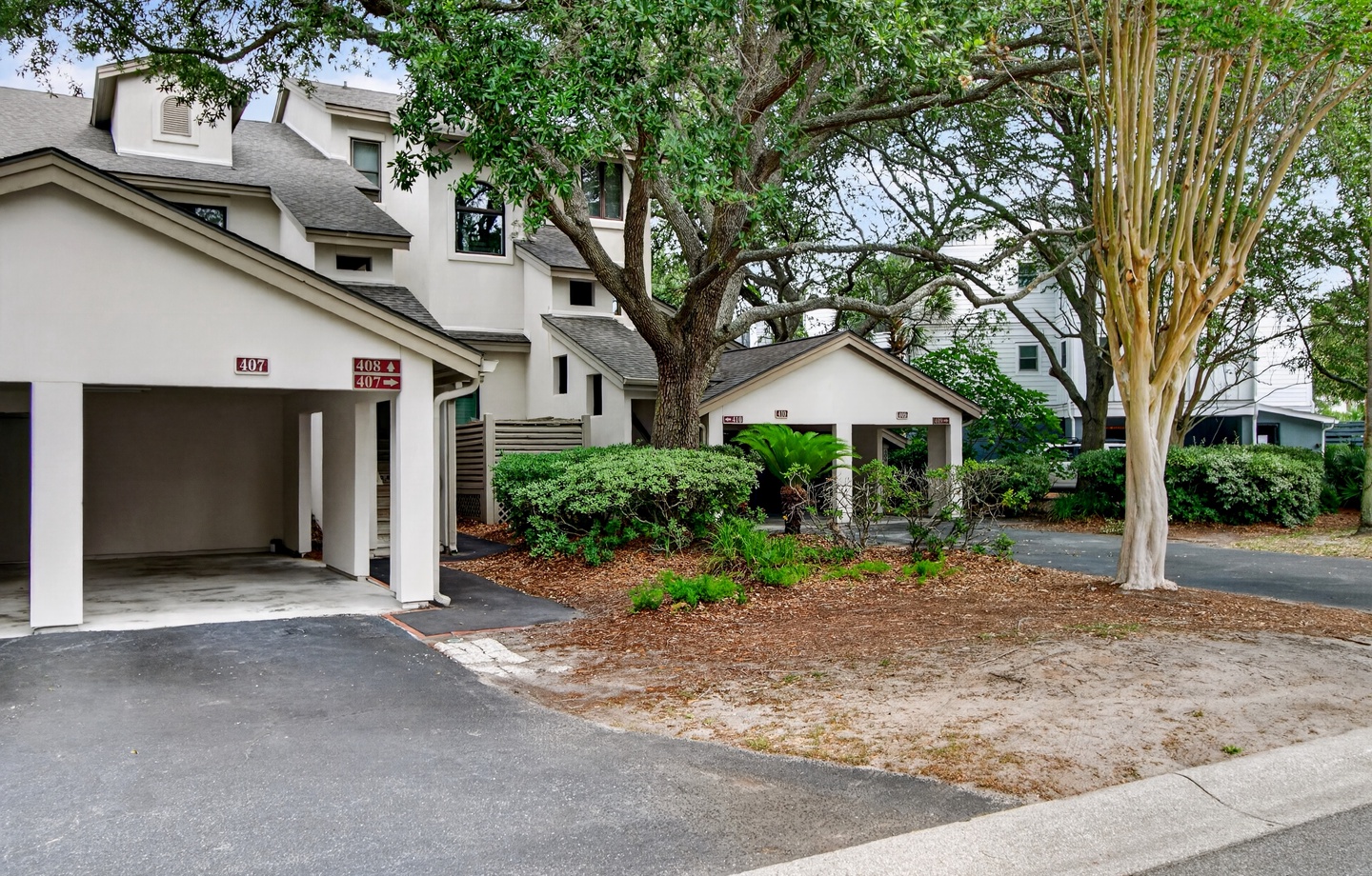 A residential complex featuring numbered units with covered carports, set among mature trees and landscaped grounds with convenient parking areas.