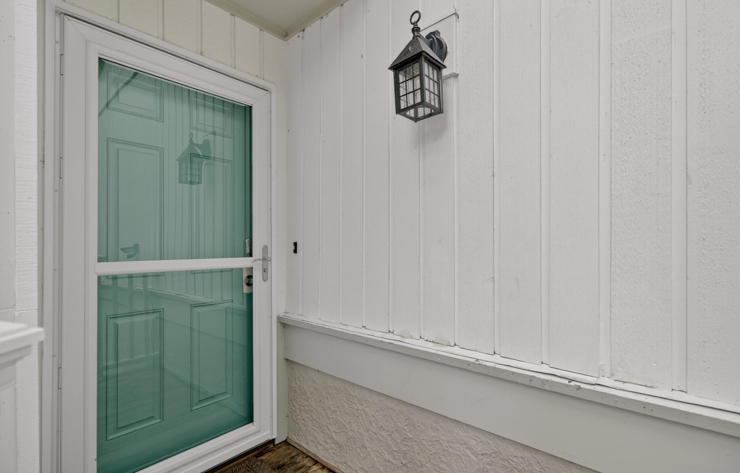 Clean, white exterior with a welcoming turquoise door and classic lantern, marking the entrance to the property.