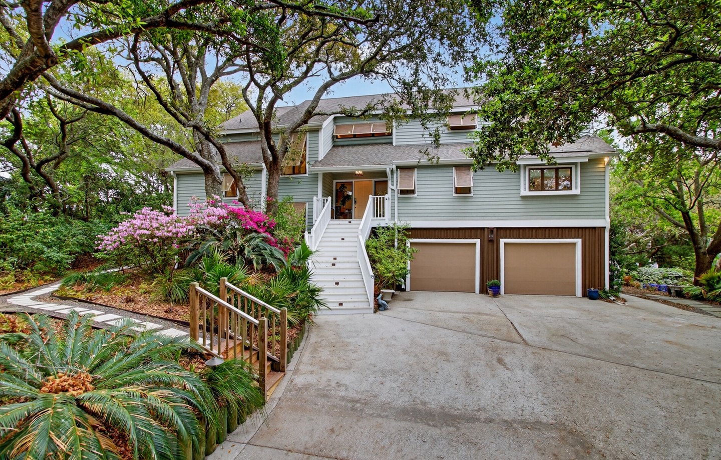 A charming coastal home nestled among mature trees with vibrant azaleas and tropical landscaping greeting your arrival.