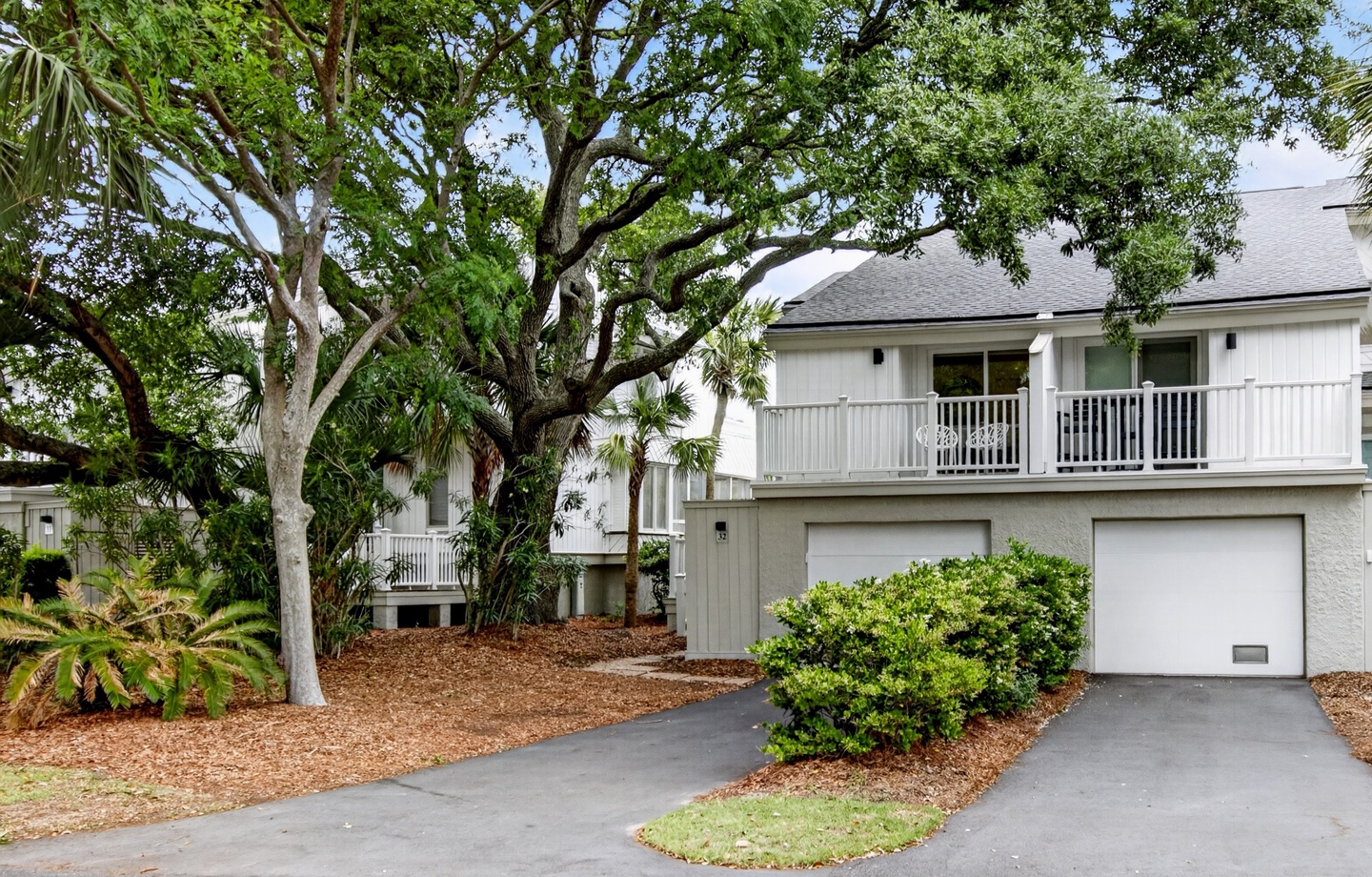 A coastal retreat framed by majestic oak trees and lush landscaping, featuring covered balconies and a two-car garage amid a peaceful residential setting.