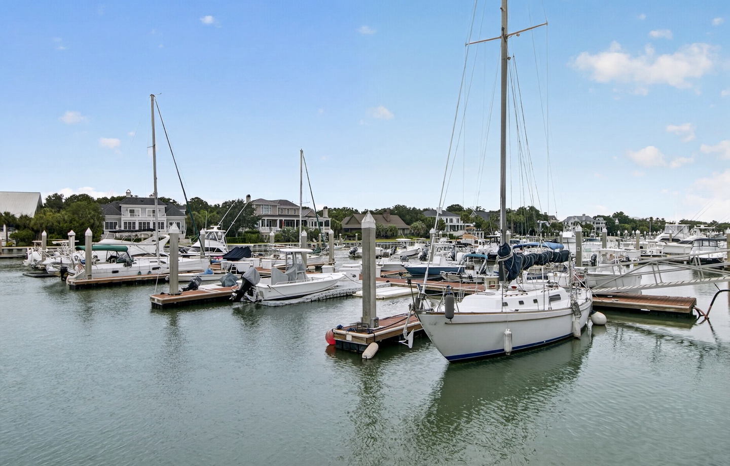 Marina views reveal a peaceful coastal neighborhood where sailboats and yachts rest along the docks, bordered by waterfront homes and trees lining the horizon.