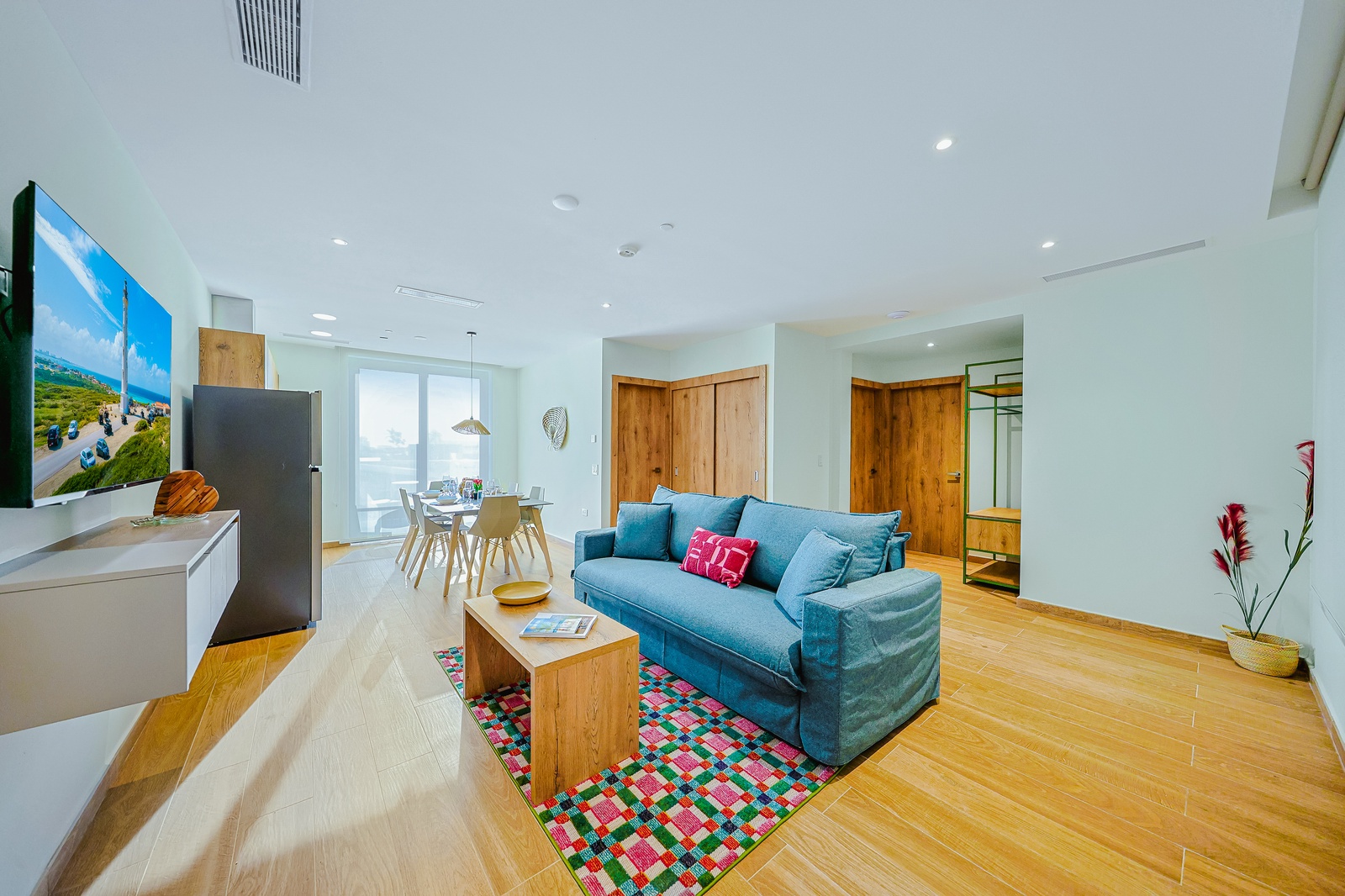 Unwind on the plush teal sofa and feel the warmth of natural light streaming through the glass doors. Bright, modern, and designed for your comfort, this open-plan space invites relaxation and easy living.
