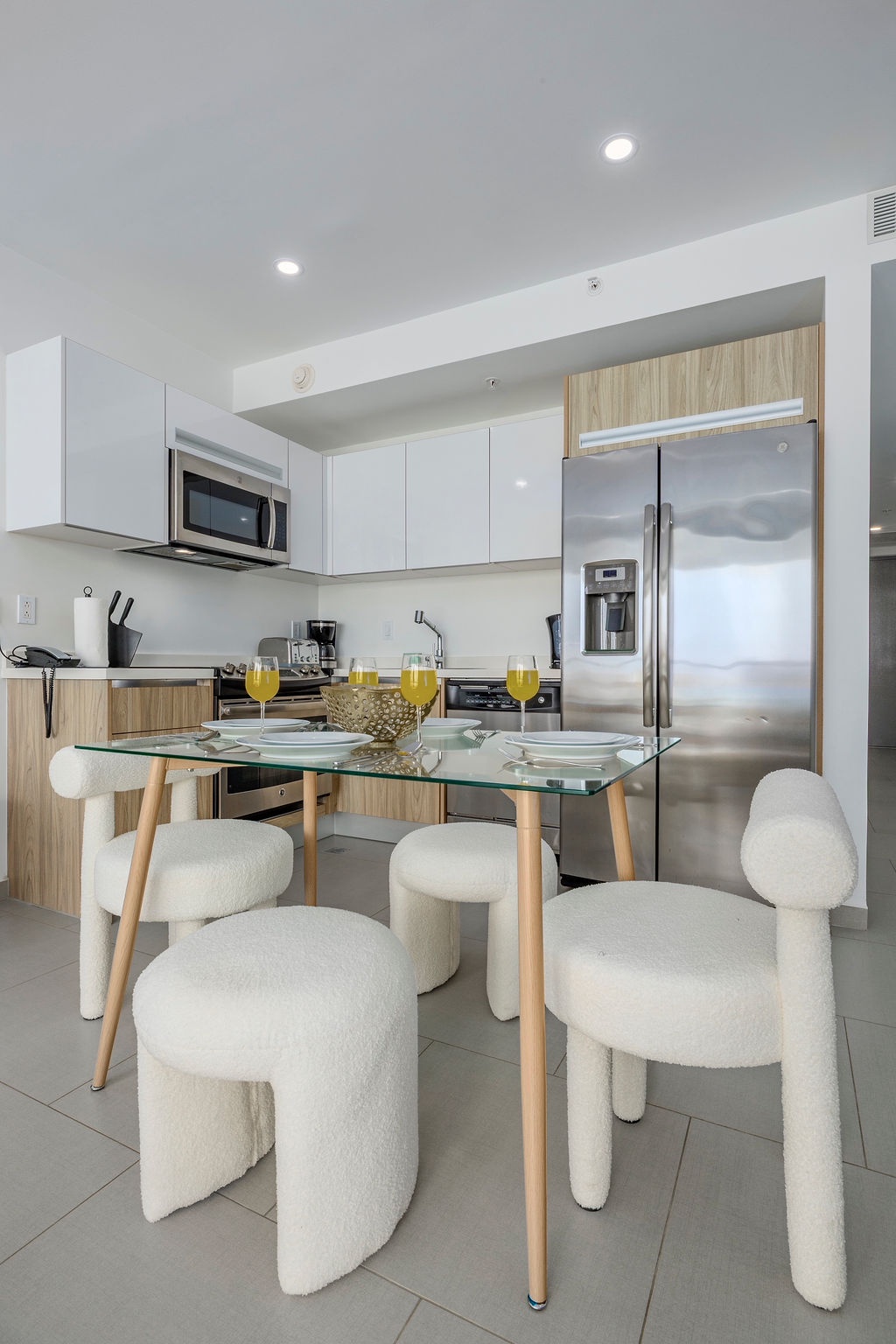 Your modern kitchen blends style and function with sleek appliances, glass dining table, and plush white chairs perfect for morning coffee.