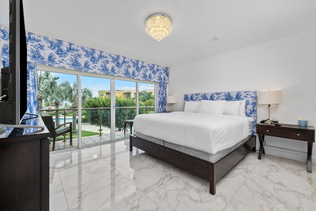 Sink into crisp white linens beneath a sparkling chandelier, with sunlit garden views framing your tranquil retreat through the sliding doors.