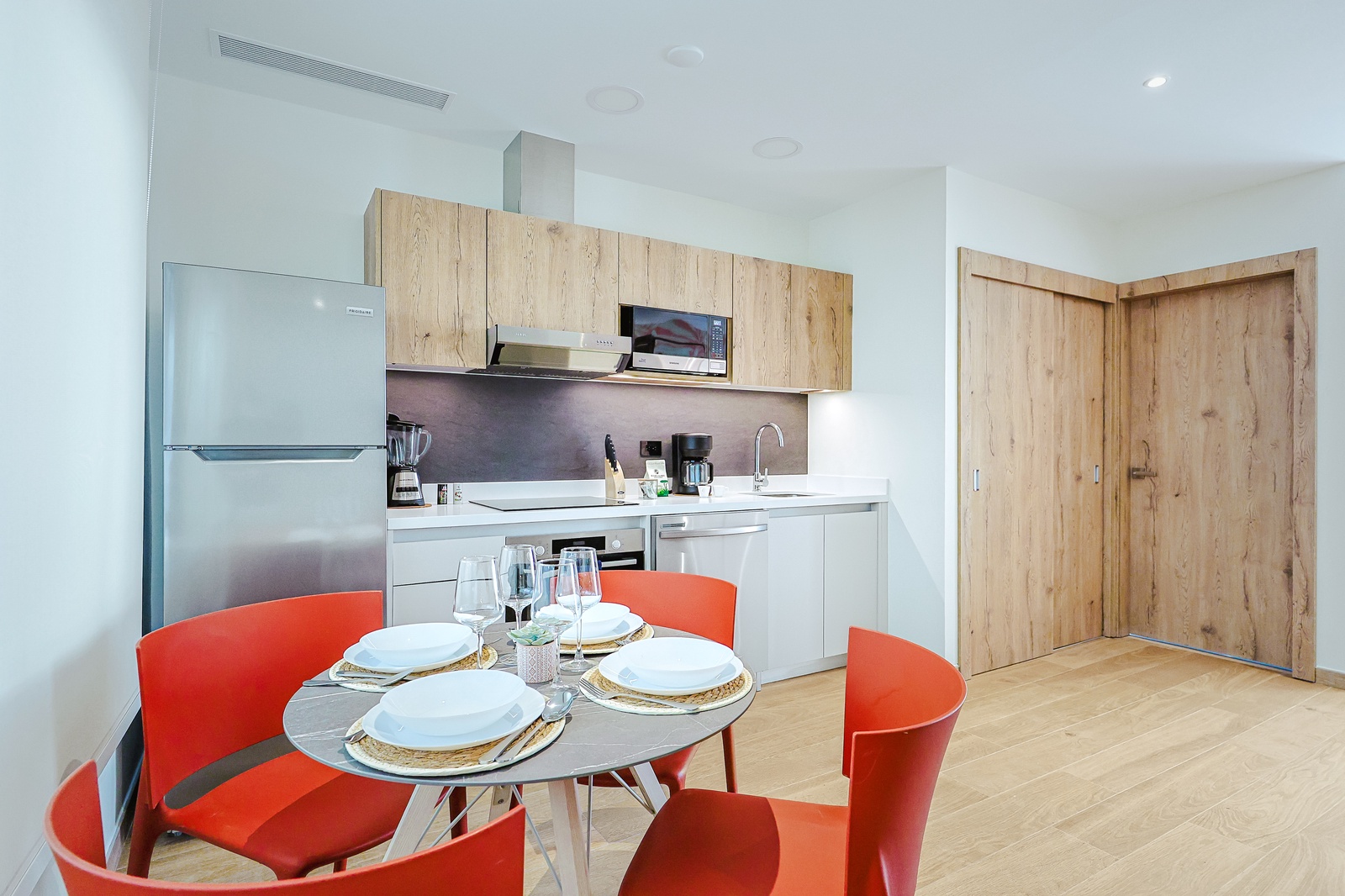 Gather around for meals in this sleek modern kitchen, featuring vibrant orange seating and contemporary wood-toned cabinetry. Your fully equipped space makes cooking easy and inviting.