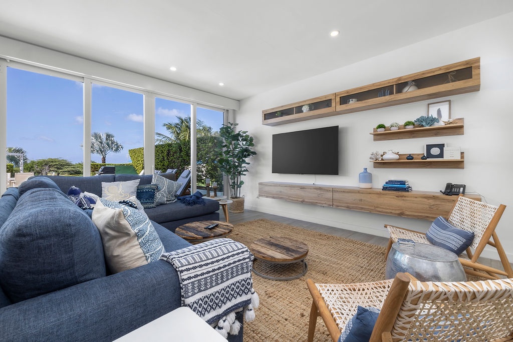 Sink into plush blue sofas while tropical breezes drift through floor-to-ceiling windows, creating your perfect retreat for relaxation and entertainment.