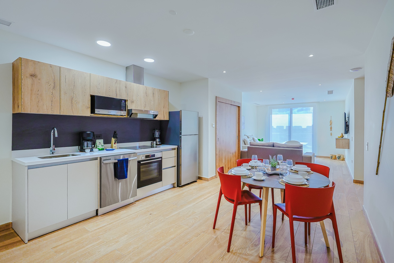 Your bright, open kitchen flows into a cheerful dining area with bold red chairs, perfect for sharing meals. Through the doorway, a cozy living space awaits with natural light streaming in.