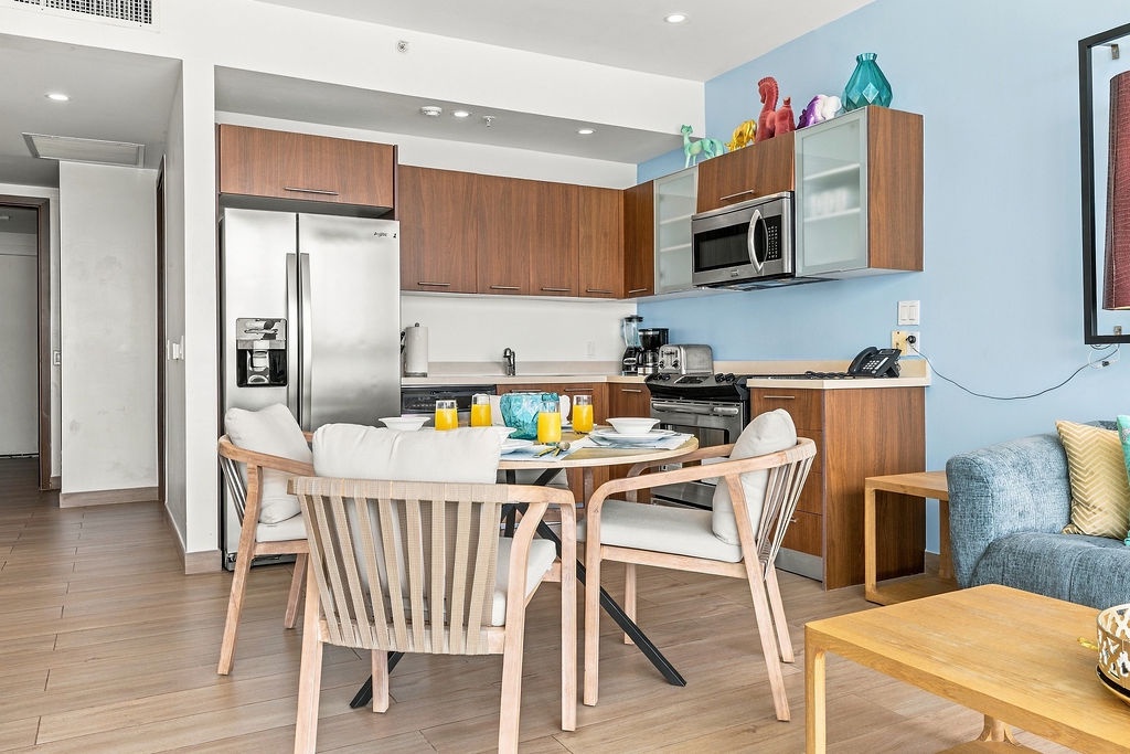 Gather around your welcoming dining table for morning coffee and fresh juice, with a fully-equipped kitchen just steps away featuring modern appliances and warm wood cabinetry.