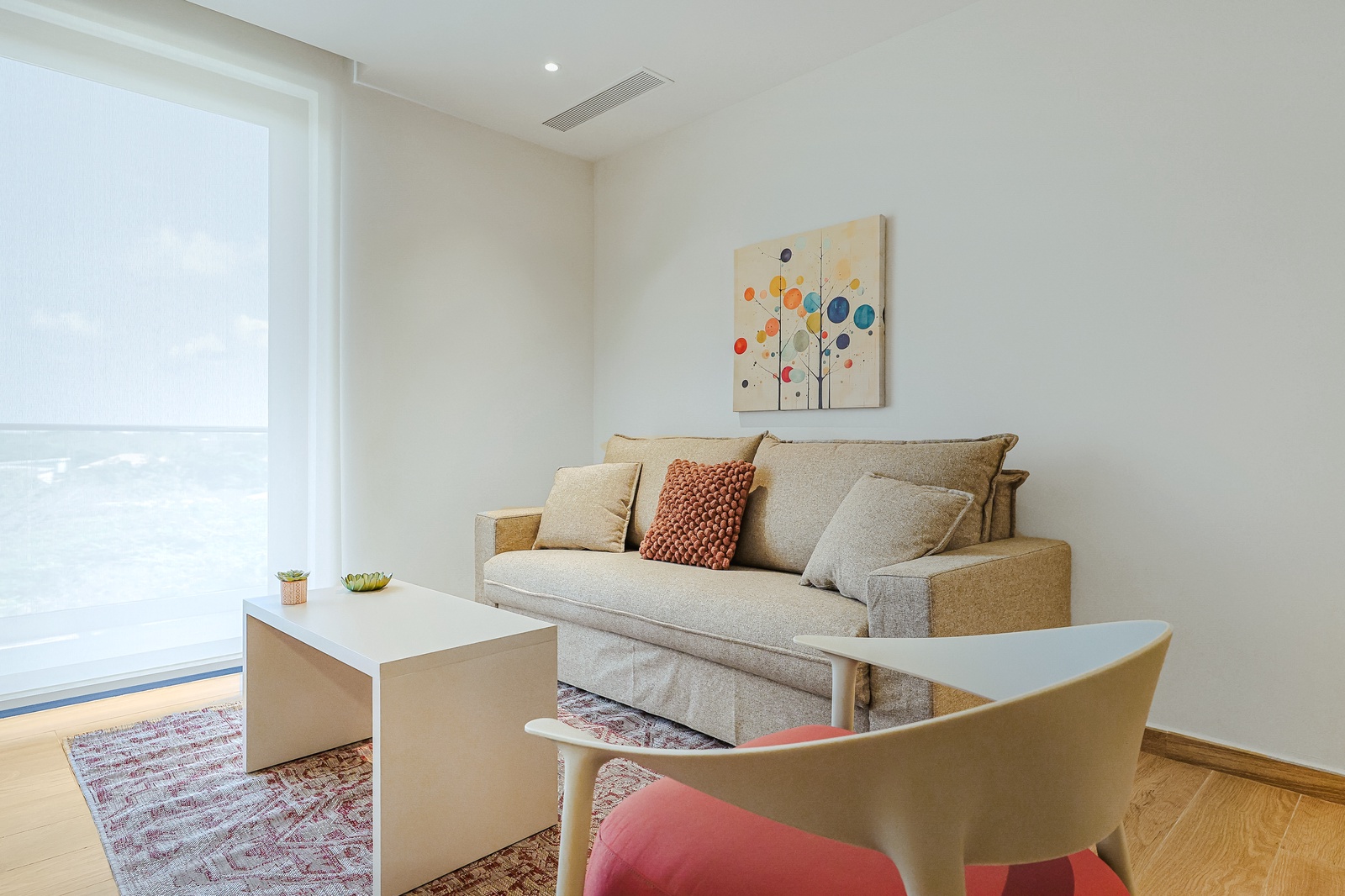 Sink into the cozy sofa, enjoy the natural light streaming through floor-to-ceiling windows, and unwind in your bright, calming living space with cheerful artwork and warm wood floors.