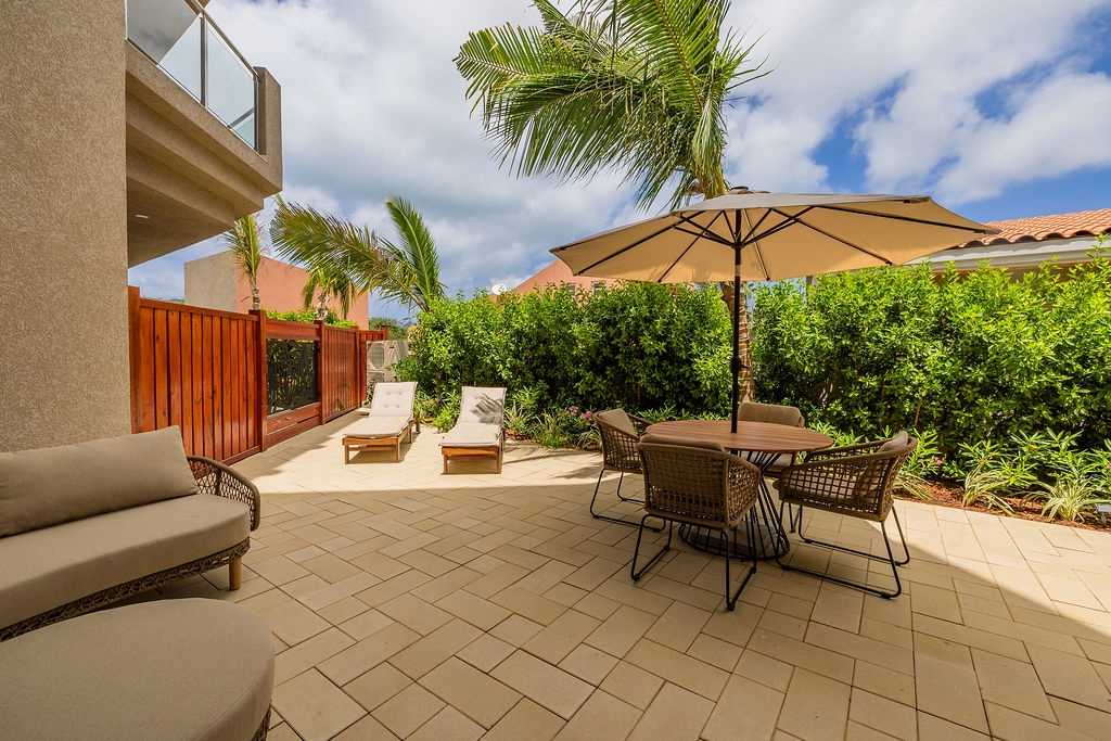 Your private patio invites you to unwind beneath swaying palms and warm sunshine, with loungers for soaking up rays, a shaded dining spot for al fresco meals, and lush greenery all around.