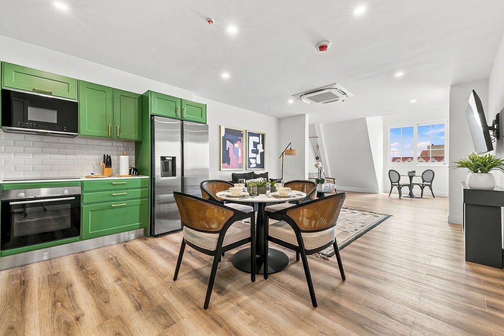 Gather around this charming dining area where vibrant green cabinetry and modern appliances set the stage for memorable meals. Bright windows frame your view while you enjoy cozy dinners or morning coffee in this inviting open-plan space.