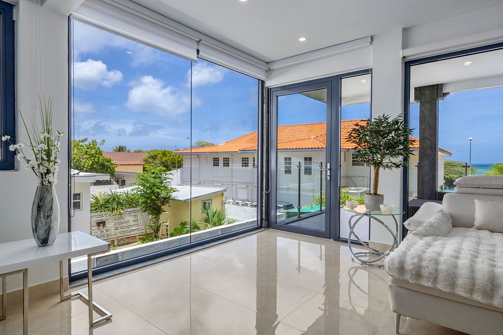 Step into this light-filled space where expansive glass doors frame stunning coastal views. Gleaming floors and crisp white walls create an airy ambiance, inviting you to relax and soak in the tropical scenery.