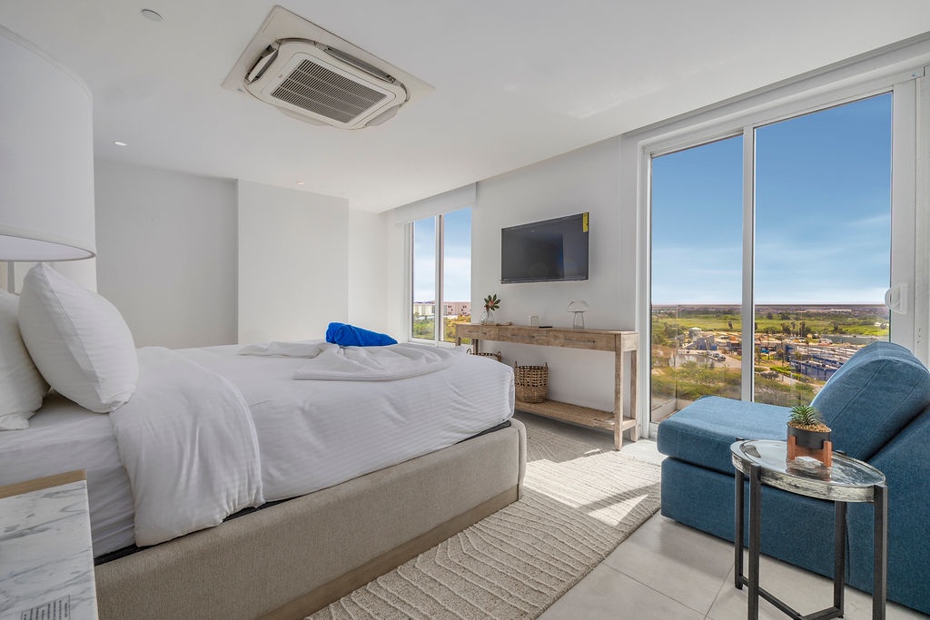 Unwind in your bright, modern bedroom with crisp white linens and a cozy reading chair. Floor-to-ceiling windows frame sweeping views you can enjoy from the comfort of your bed.