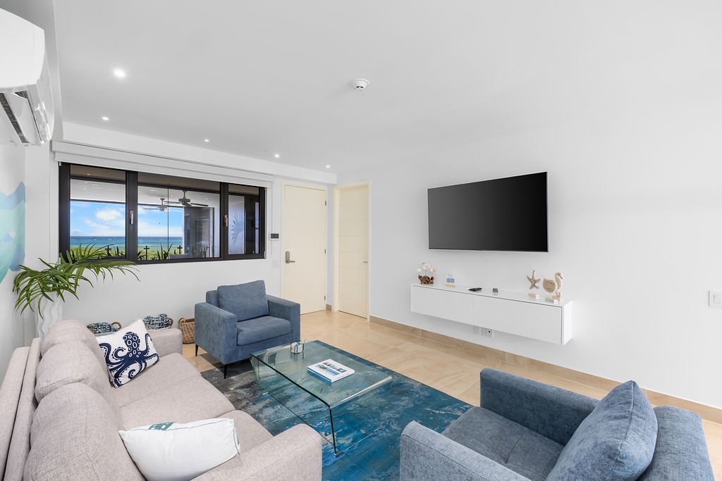 Unwind in your bright, modern living space with plush seating, a smart entertainment setup, and ocean breezes flowing through. The minimalist design and coastal touches create the perfect backdrop for your seaside escape.