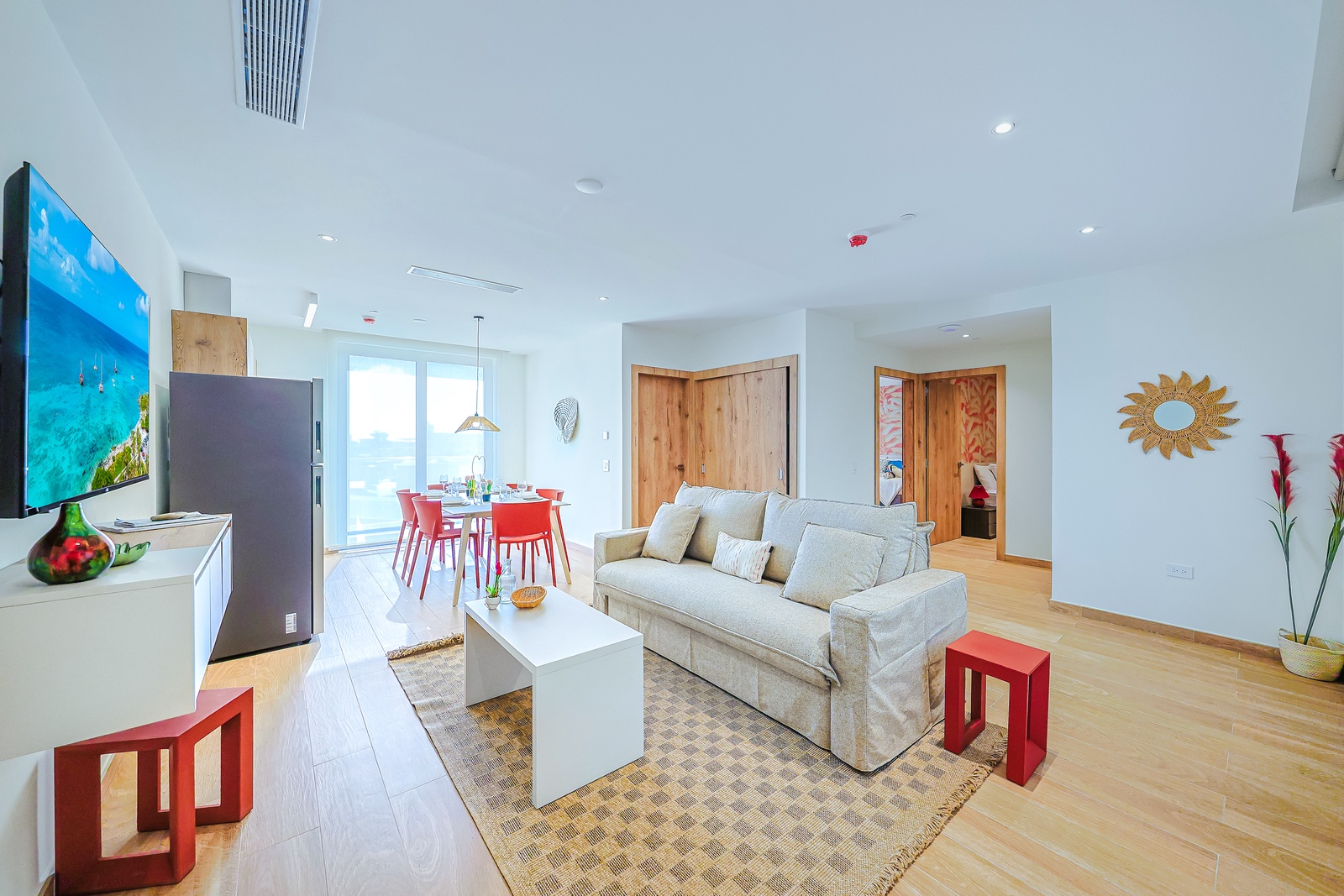 Step into this bright, open-plan living space where sunshine streams through floor to ceiling windows. Plush seating, pops of color, and warm wood floors invite you to settle in and enjoy your island getaway.