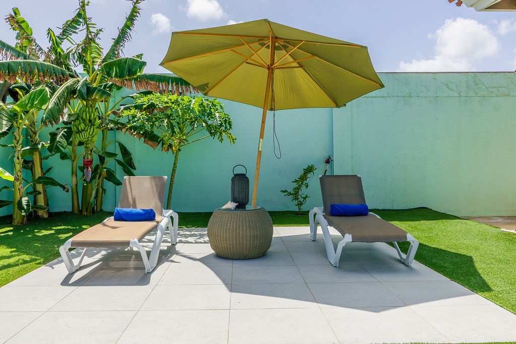 Your private sunlit patio invites relaxation—lounge on comfortable sunbeds beneath a bright umbrella, surrounded by tropical greenery and the gentle warmth of sunshine.