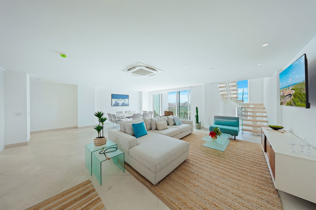 Step into your bright, open living space where contemporary comfort meets coastal style. Natural light streams through floor-to-ceiling windows, while pops of turquoise invite you to unwind on plush seating after your island adventures.