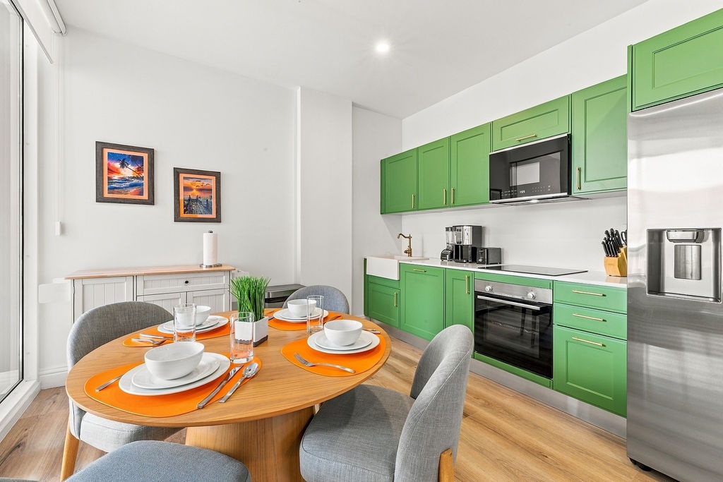 Your bright kitchen and dining space awaits with cheerful green cabinetry, modern appliances, and a welcoming table set for your first meal.