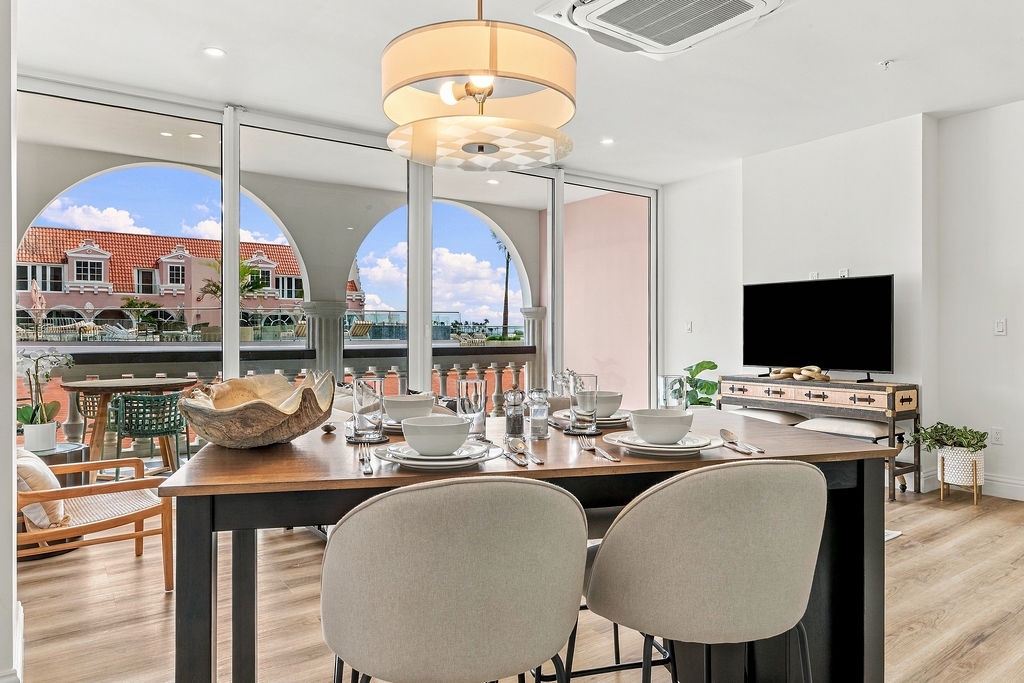 Gather with loved ones around this sleek dining table, where sunlight pours through arched windows framing waterfront views. Your perfectly set table waits, inviting laughter and unforgettable meals.