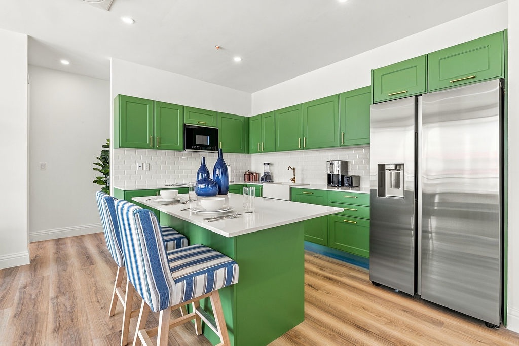Step into a bright, modern kitchen with bold green cabinetry and sleek stainless appliances. Gather at the island for morning coffee or meal prep, with everything you need right at your fingertips for a comfortable stay.