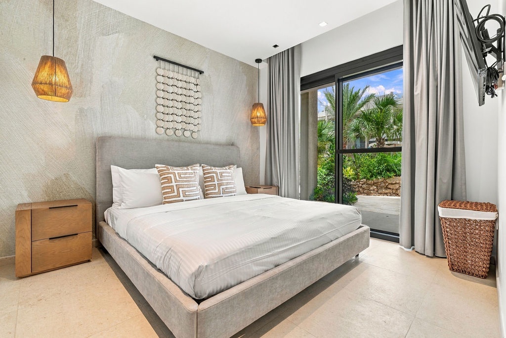 Sink into crisp linens in your serene bedroom, where natural light and lush garden views through floor-to-ceiling windows create your perfect retreat after a day of exploring.