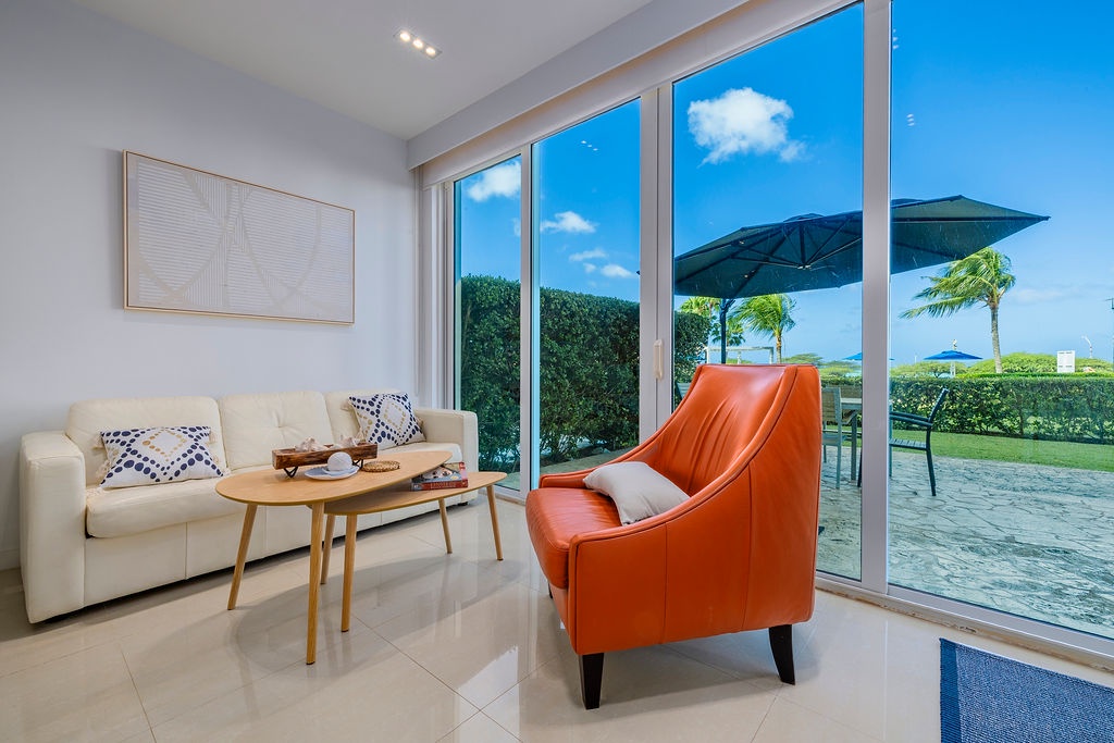 Settle into your bright living room where floor-to-ceiling windows frame tropical paradise. Your comfortable seating overlooks lush gardens and swaying palms.